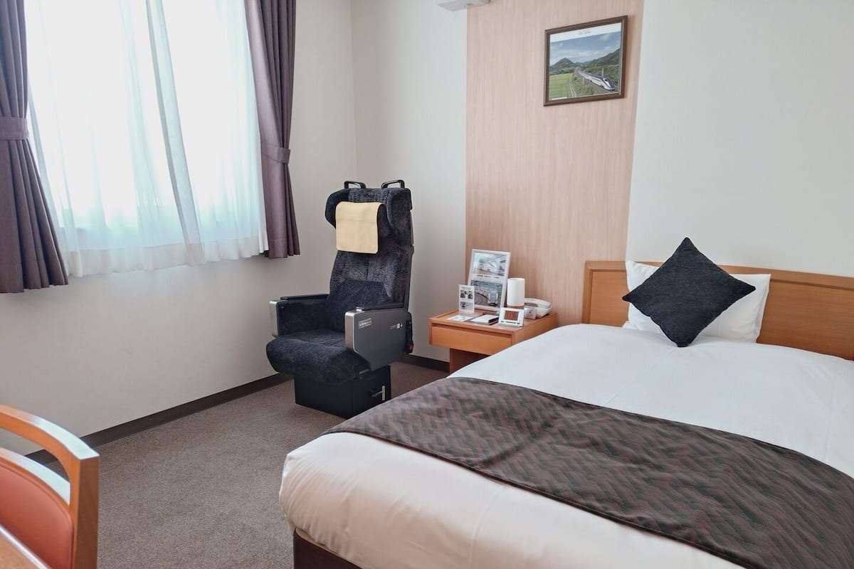 Ein Hotelzimmer mit Bett, Stuhl, Nachttisch und einem Fenster mit Vorhängen.