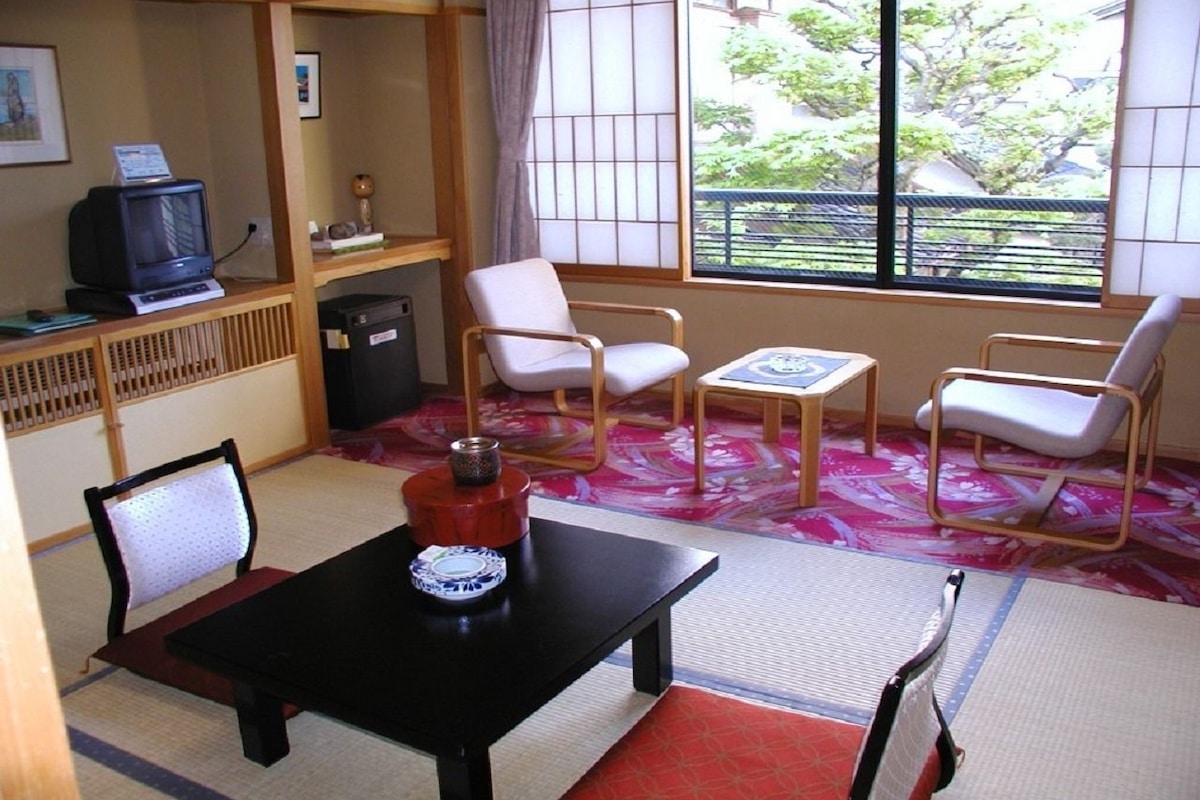 A traditional Japanese-style room with tatami flooring, a low table, and a television on a shelf.
