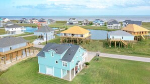 A coastal residential area with houses on stilts near a body of water, featuring a mix of single and multi-story buildings.