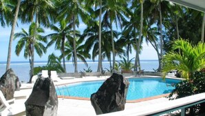 A pool with large rocks, surrounded by palm trees and a view of the ocean. - Sunhaven Beach Bungalows (Rarotonga)