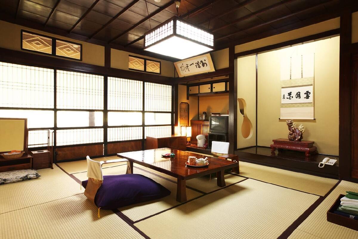 A traditional Japanese room with tatami flooring, a low table with a tea set, a television, and a guitar.
