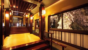 A wooden staircase with a tatami mat floor leading to a room with a large window displaying cherry blossoms. - Nishiya (Yonezawa)