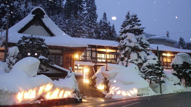 A snow-covered building with a traditional design, a staircase leading to the entrance, and snow-covered trees. - Nishiya (Yonezawa)