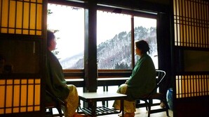 A traditional room with tatami flooring, a low table, and a view of a snowy landscape through large windows. - Nishiya (Yonezawa)