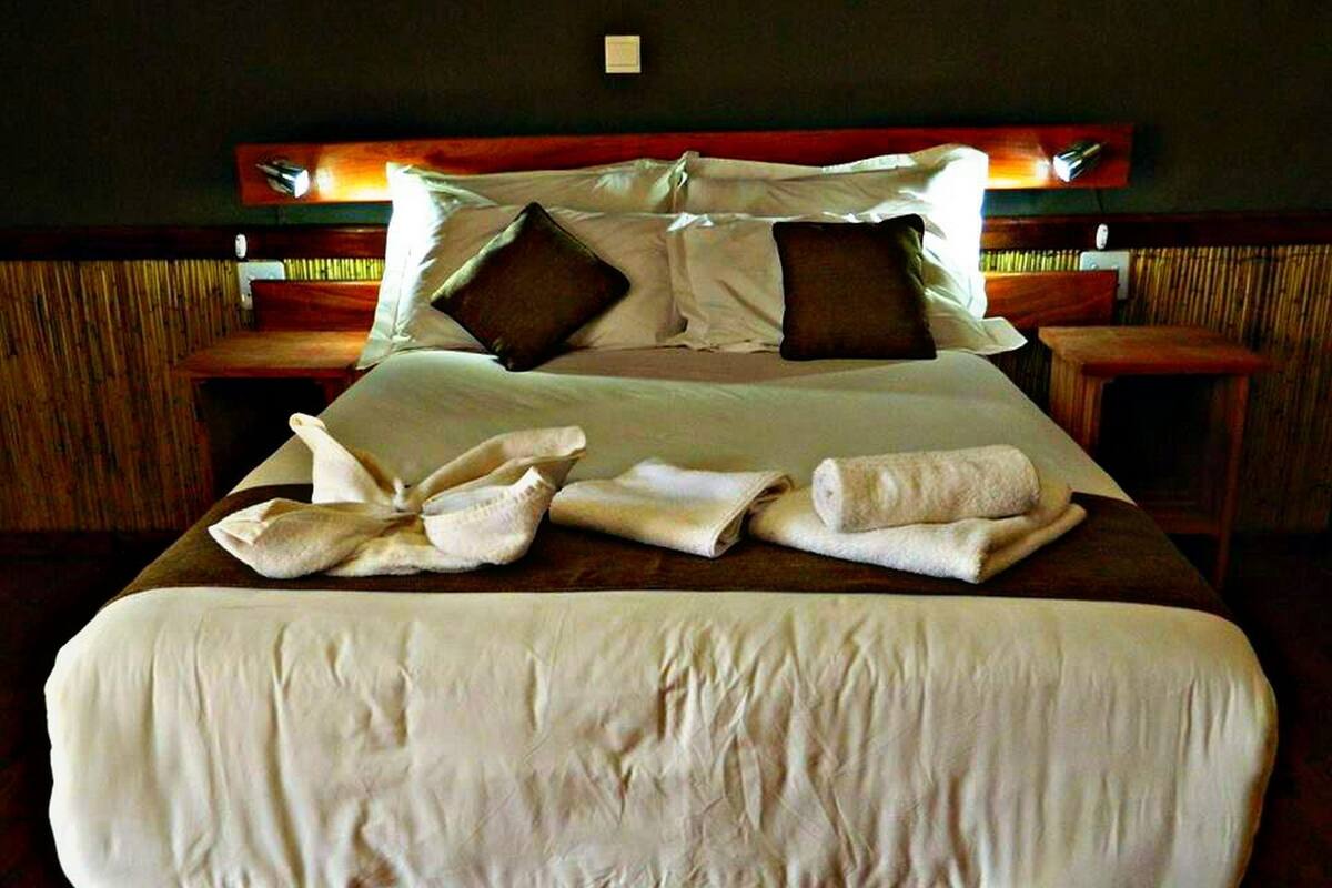A neatly made bed with pillows, a folded towel, and a rolled towel on a wooden headboard.