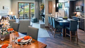 A modern hotel room with a dining area, kitchen, and a balcony with a scenic view.