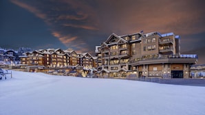 A multi-story hotel with a ski resort in the background, featuring a prominent entrance and multiple balconies.