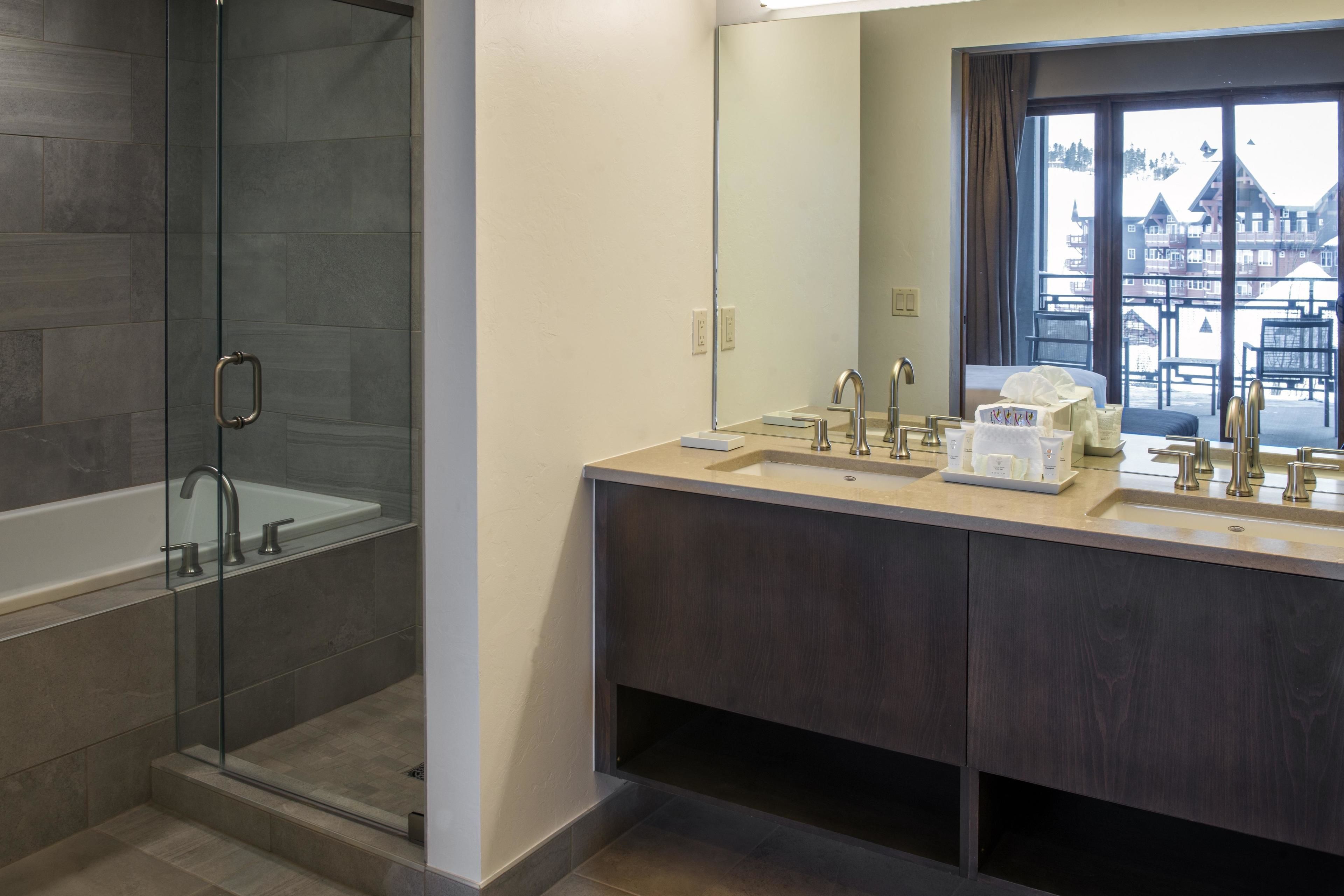 Un baño moderno con ducha envuelta en vidrio, un espejo grande y una ventana que ofrece vistas a un edificio.