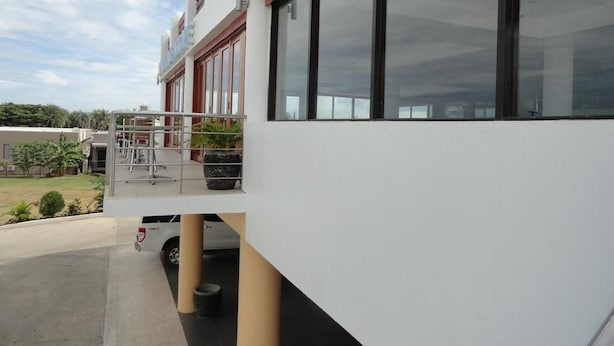 Een modern gebouw met grote ramen, een overdekt terras en een wit voertuig ervoor geparkeerd.