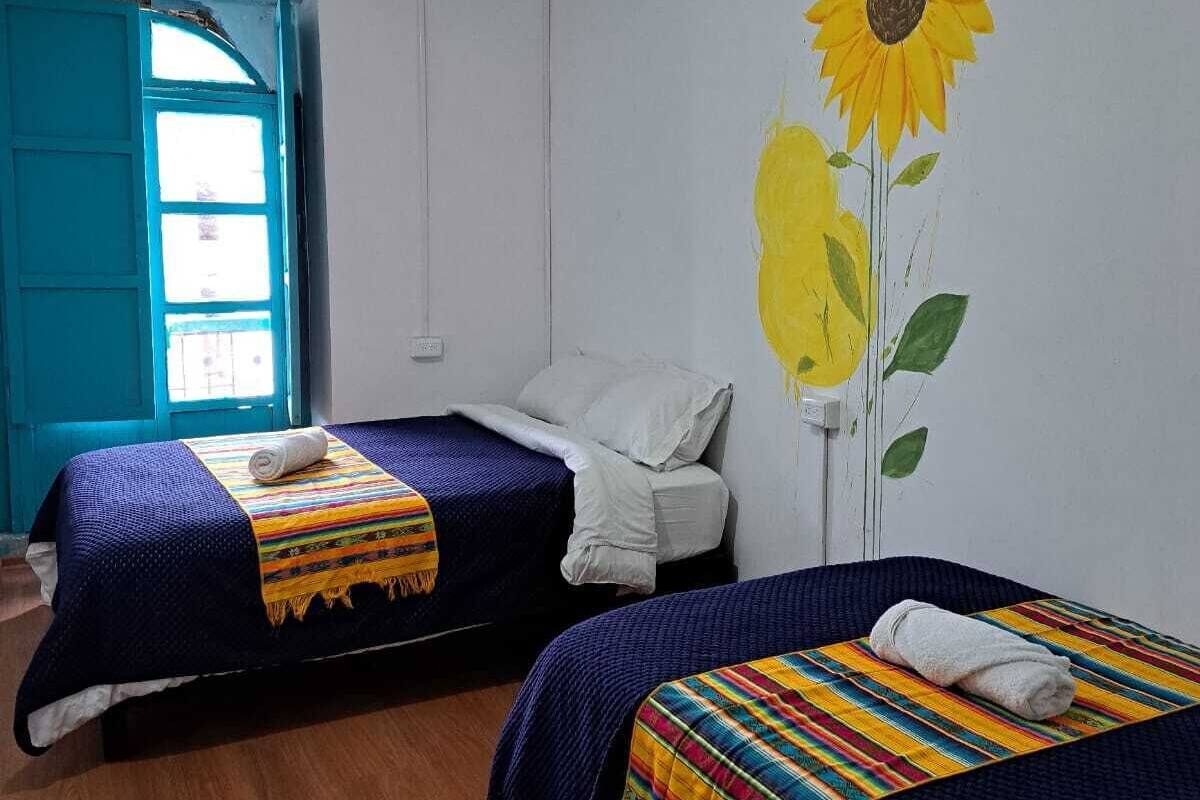 A room with two beds, a large window, and a sunflower mural on the wall.