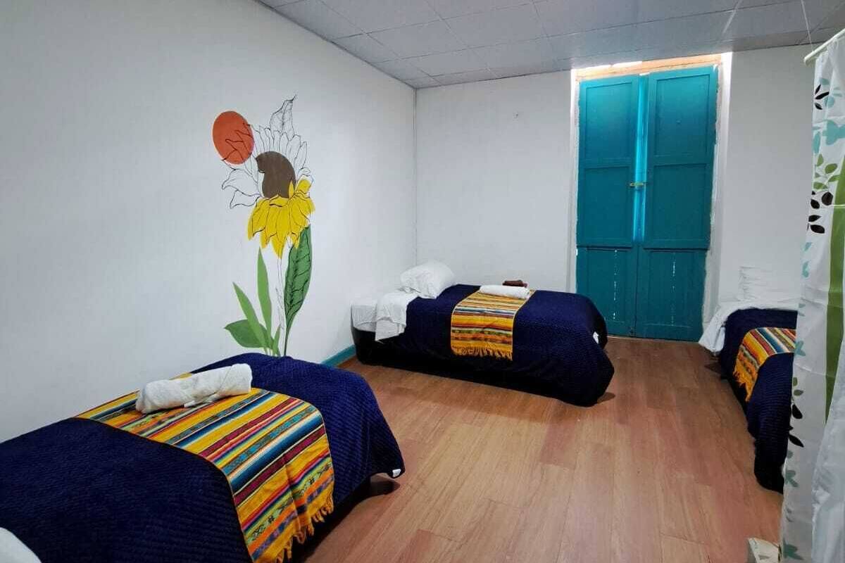 A room with two beds, a mural, a blue door, and a wooden floor.