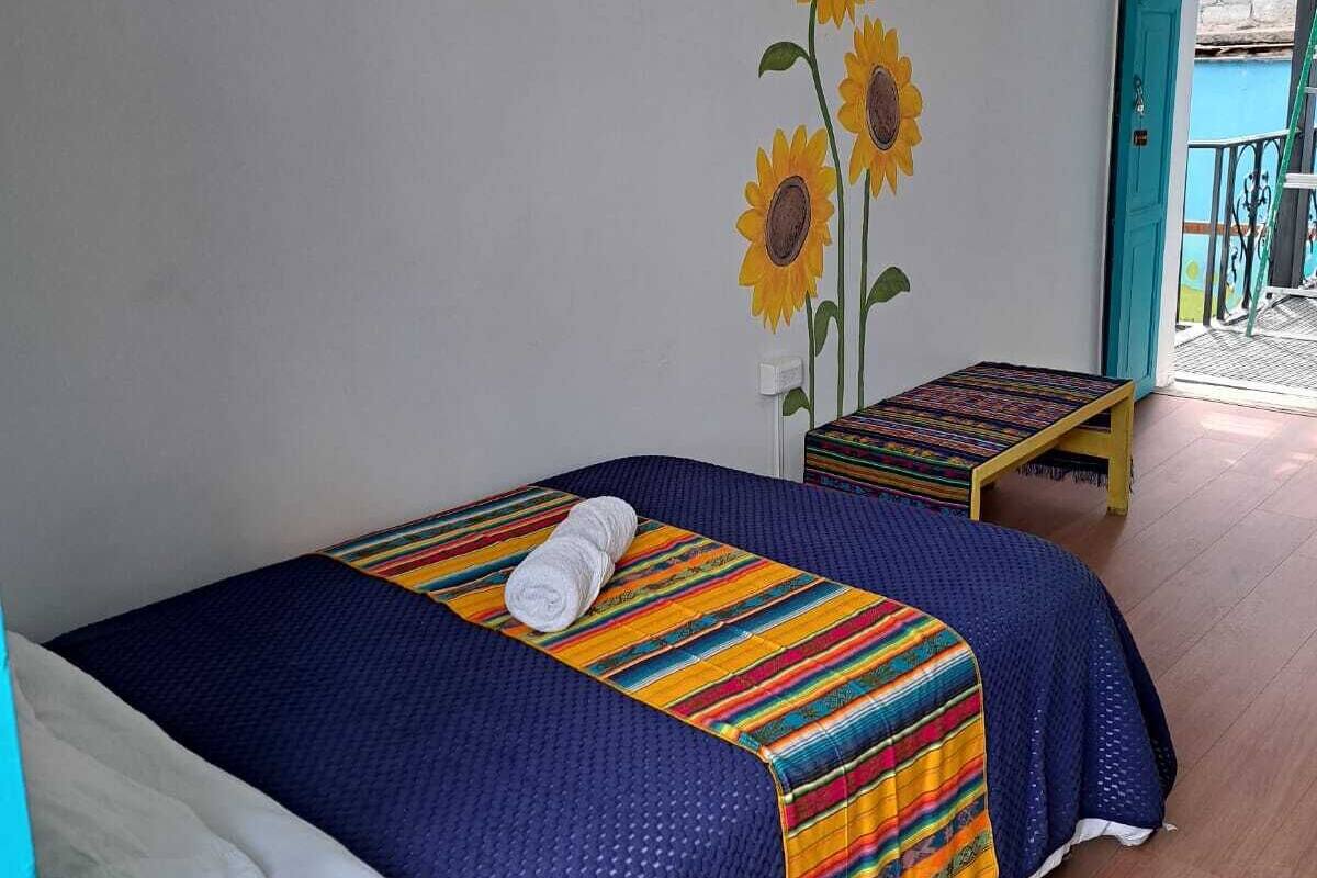 A room with a bed, a colorful striped blanket, a towel, and a small stool.