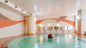 A swimming pool with a central sculpture, multiple shower heads, and a tiled wall with a geometric pattern.