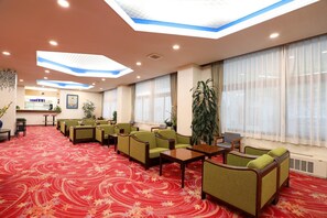 A hotel lobby with a red carpet, green sofas, a reception desk, and large windows with sheer curtains.