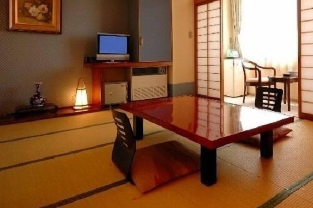 A traditional Japanese room with tatami flooring, a low table, a television, and sliding doors.