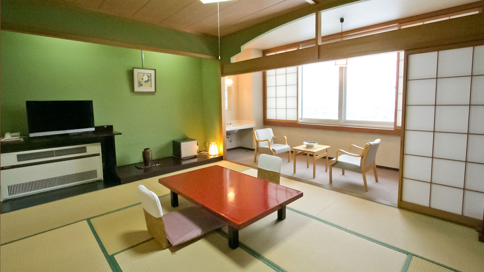 A room with tatami flooring, a television, a desk, chairs, and a large window.