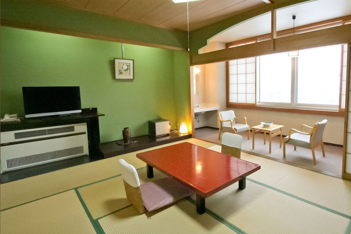 A room with tatami flooring, a television, a desk, chairs, and a large window.