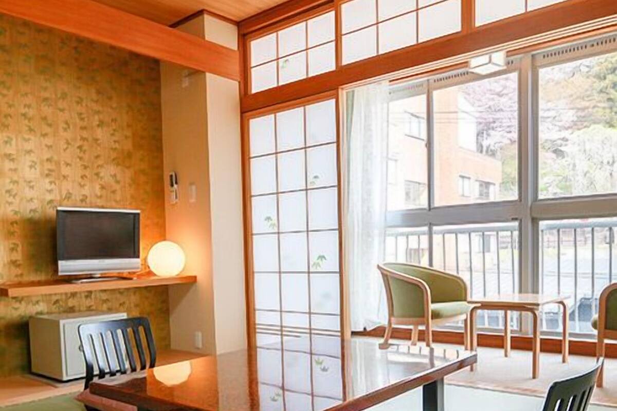 A traditional Japanese room with tatami flooring, a low table, a television, and a view of the outside.