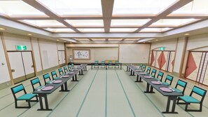Un salón de conferencias con mesas largas y sillas, techo con tragaluces y una obra enmarcada en la pared.