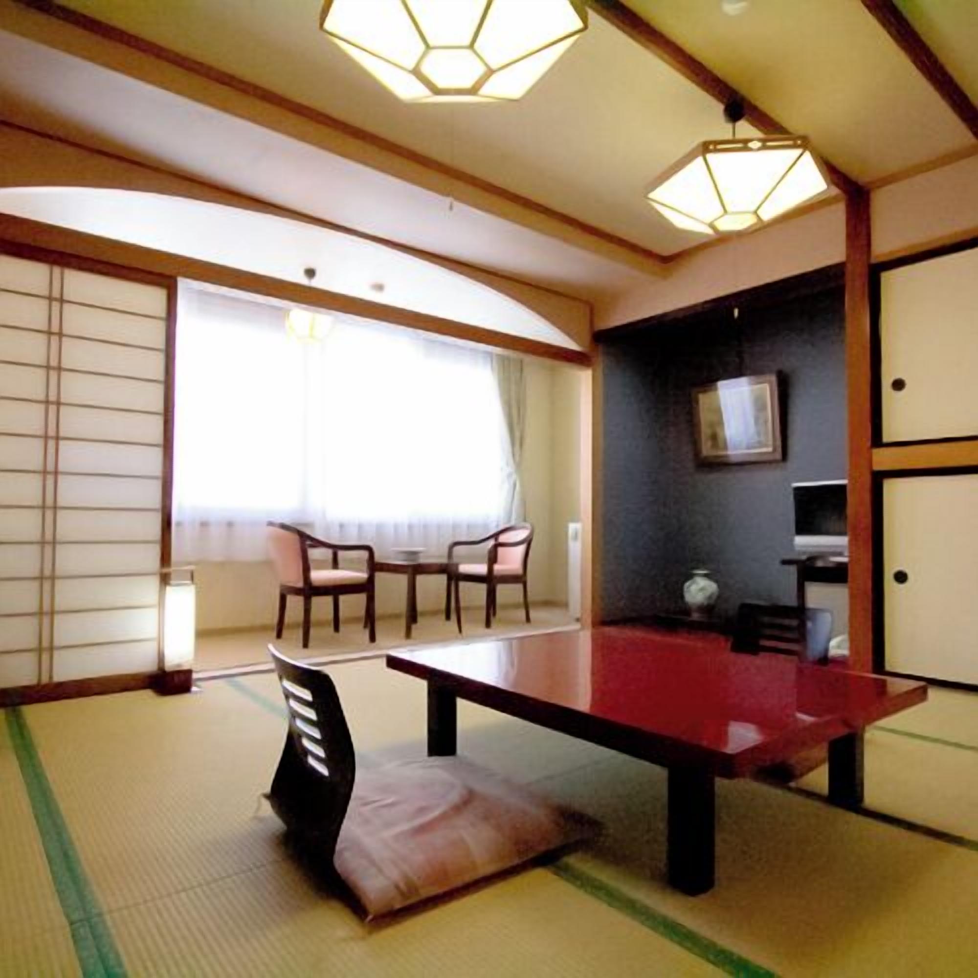 A traditional Japanese room with tatami flooring, a low table, chairs, a sliding door, and a ceiling light fixture.