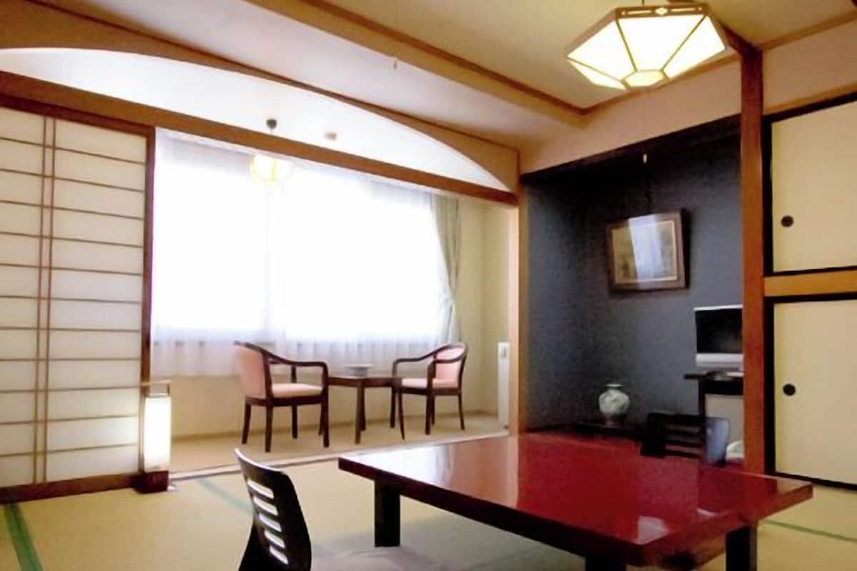 A traditional Japanese room with tatami flooring, a low table, chairs, a sliding door, and a ceiling light fixture.