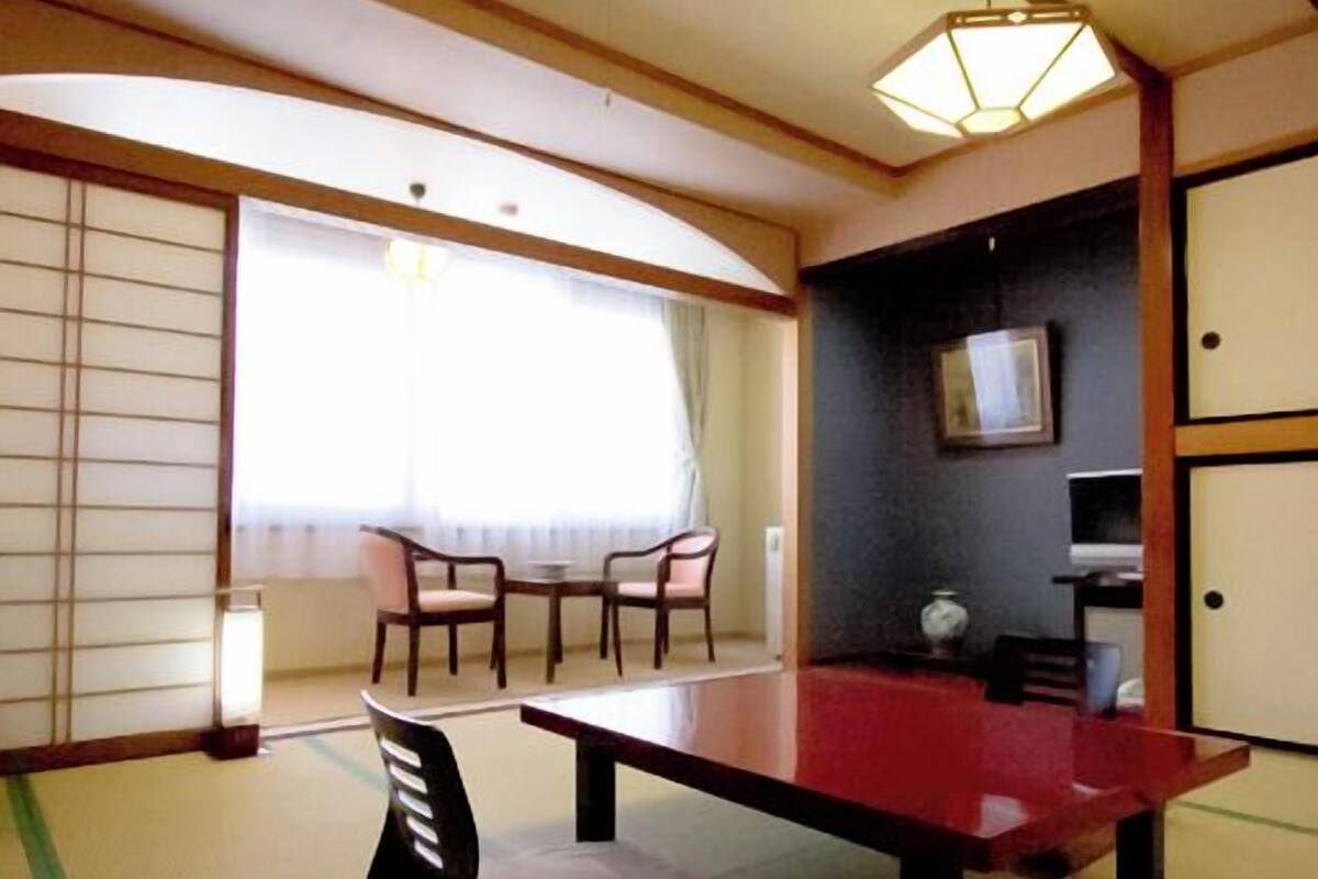 A traditional Japanese room with tatami flooring, a low table, chairs, a sliding door, and a ceiling light fixture.