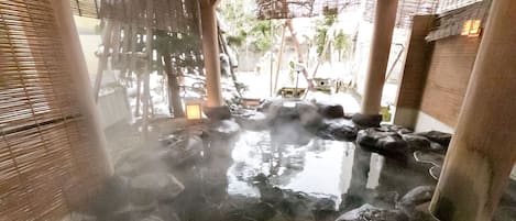 A hot spring area with stone steps leading into a pool, bamboo blinds, and a wooden structure.