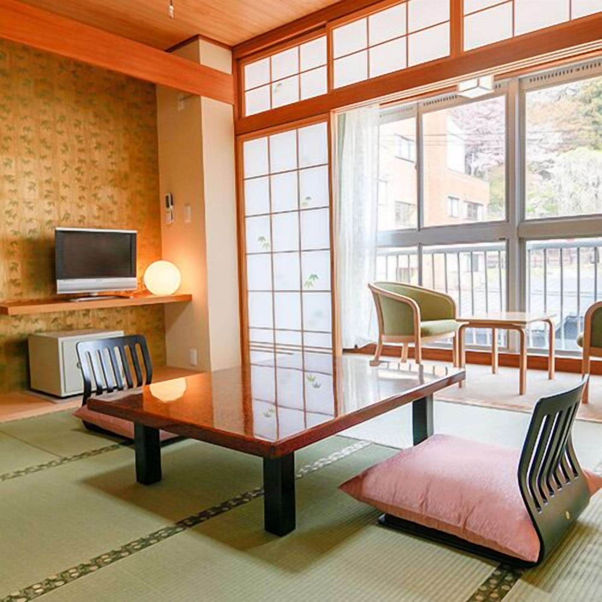 A traditional Japanese room with tatami flooring, a low table, a television, and a view of the outside.