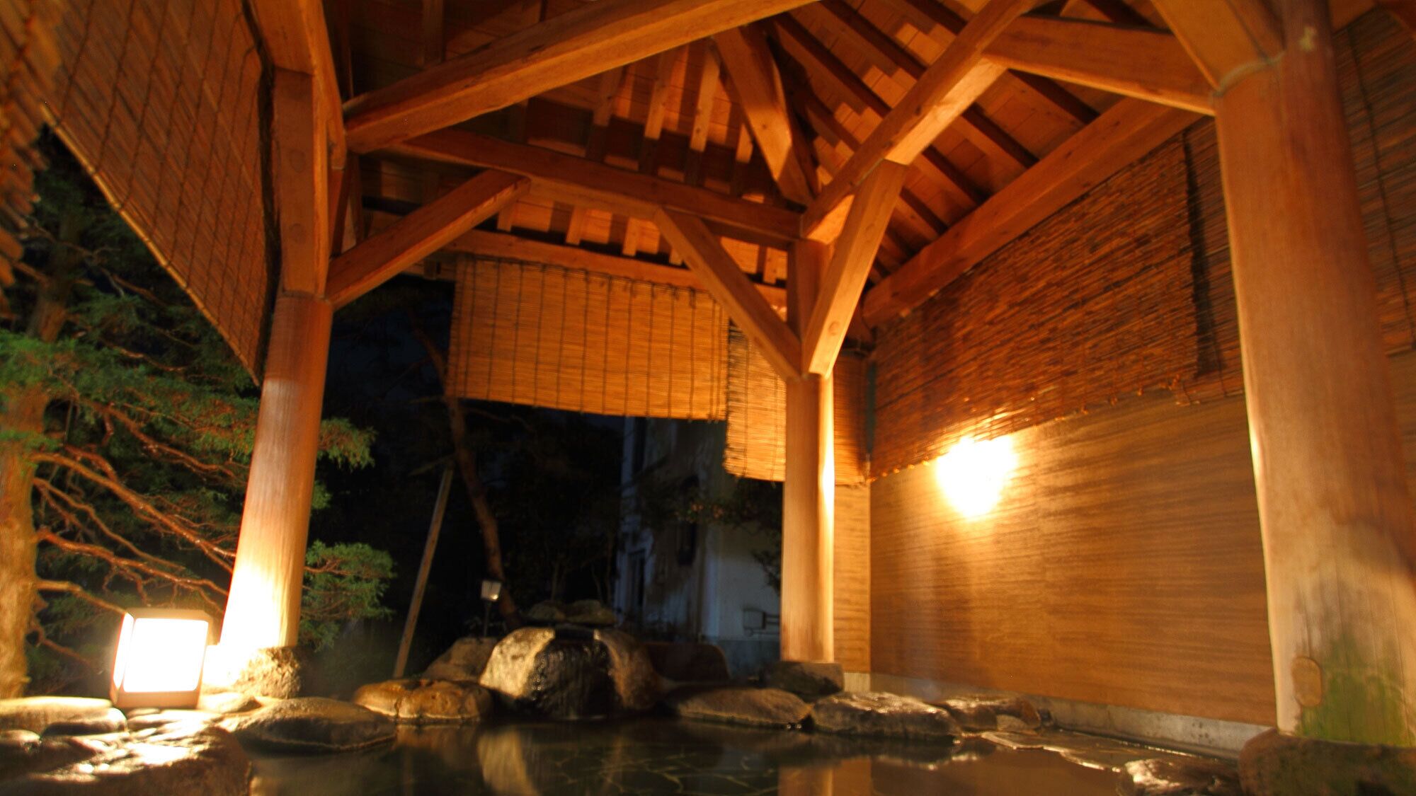 A traditional wooden structure with a thatched roof, a stone water feature, and a bamboo screen.