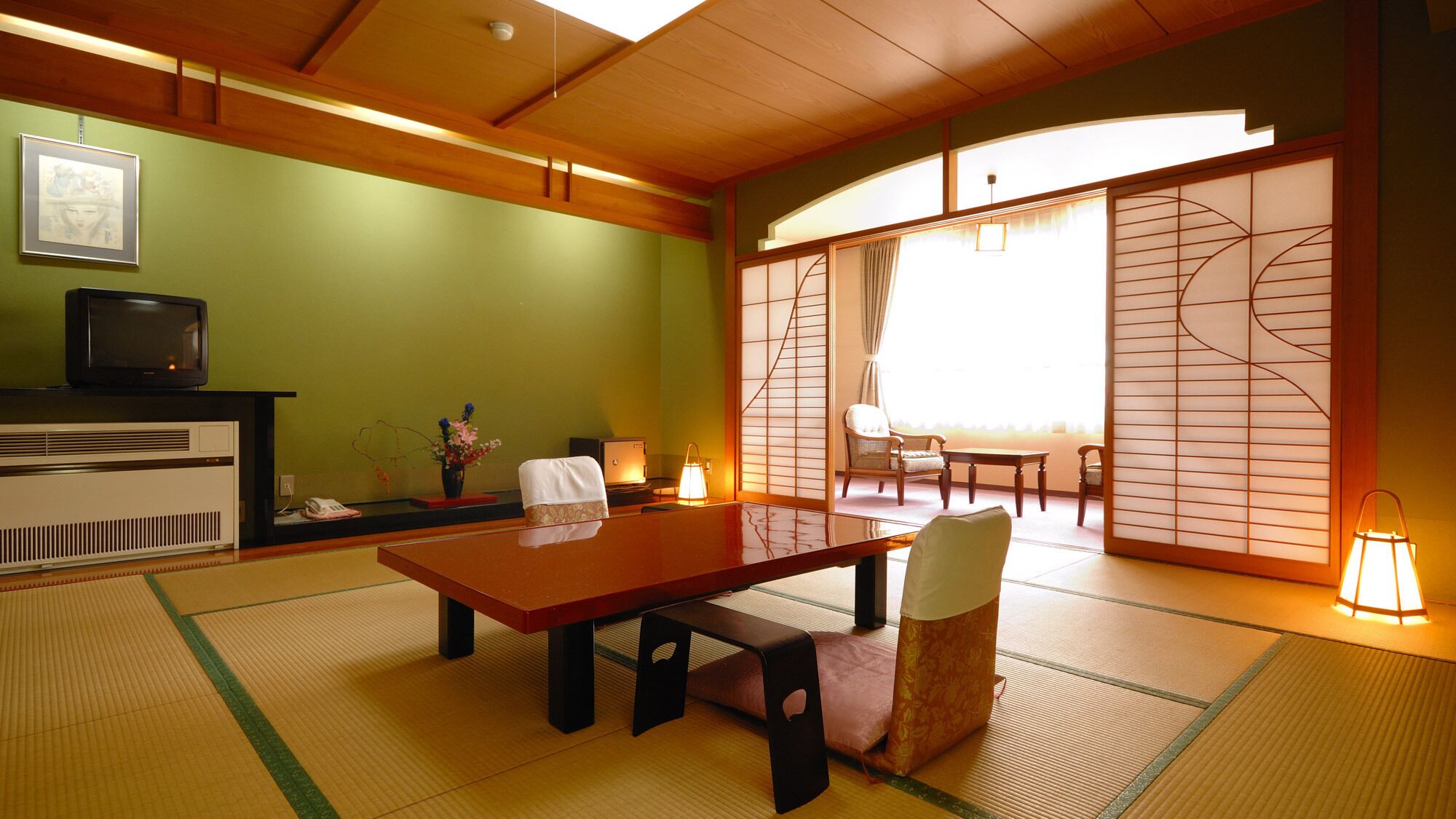 A traditional Japanese room with tatami flooring, a low table, chairs, a television, and sliding doors.