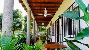 A covered outdoor area with a ceiling fan, columns, and potted plants.