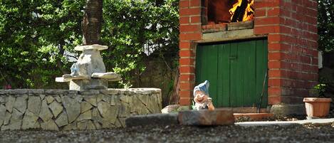 A brick outdoor oven with a green door, surrounded by a stone wall and a tree.