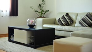 A living room with a black coffee table, a white sofa with striped pillows, a potted plant, and a glass vase with flowers. - Green Garden apartment (Split)