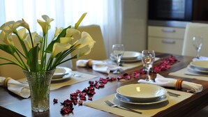 A dining table set for four with white plates, glasses, and a vase of white flowers. - Green Garden apartment (Split)