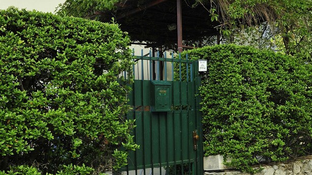 A gated entrance with a stone wall and a green gate, leading to a building with a beige facade and a balcony. - Green Garden apartment (Split)