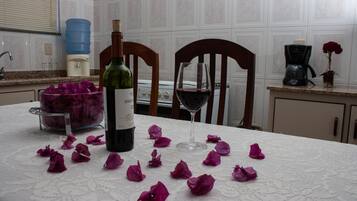 A kitchen with a table set for a romantic dinner, featuring a bottle of wine, a glass of red wine, and scattered rose petals.