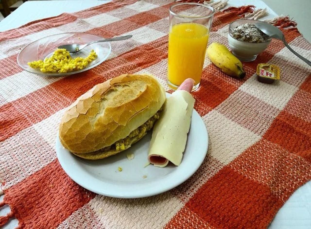 A meal consisting of a sandwich, a rolled item, a glass of orange juice, and a banana on a checkered tablecloth.