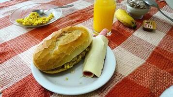 A meal consisting of a sandwich, a rolled item, a glass of orange juice, and a banana on a checkered tablecloth.