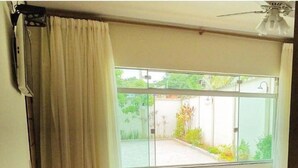 A room with a bed, a table with a vase of flowers, and a window with a view of greenery. - Apart Hotel Água Limpa (Prados)
