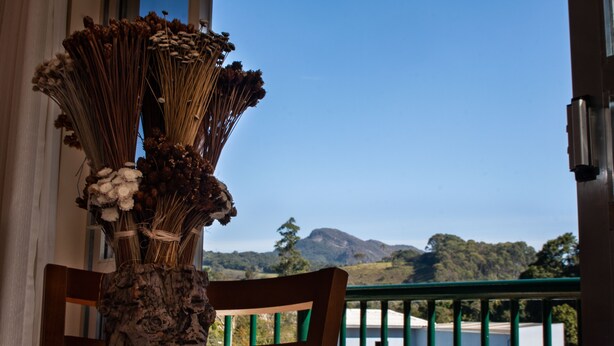 A table with a vase of dried flowers and a wooden chair. - Apart Hotel Água Limpa (Prados)