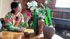 A person sitting at a wooden table with a vase of flowers and a teapot. - Dong Que Homestay-Tours-Motorbike, Car rental, Hiking (Ha Giang 1)