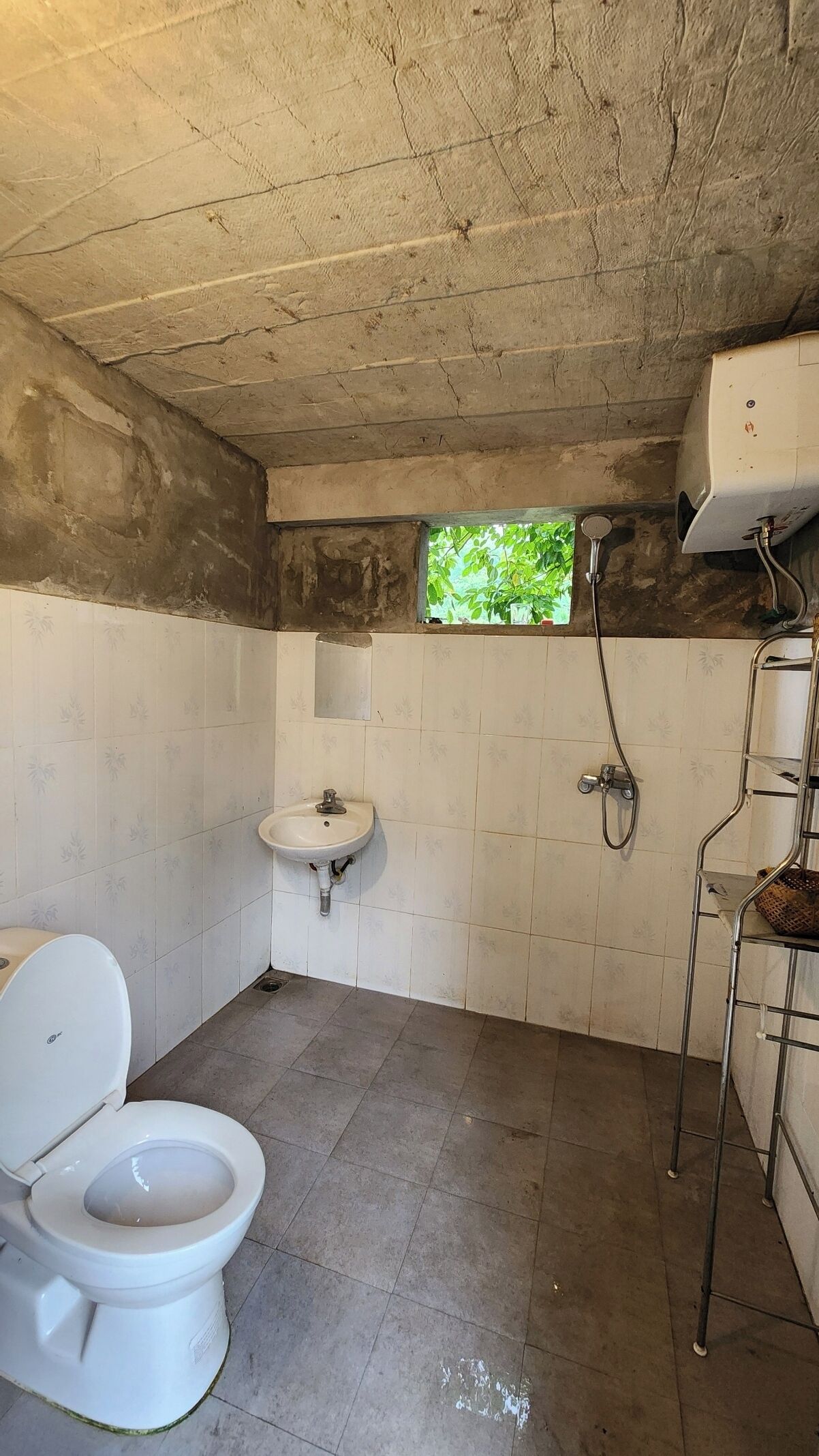 A bathroom with a toilet, sink, shower, and a small window.