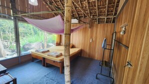 A room with a bed, a bamboo pillar, a mosquito net, a metal rack, and a view of the outdoors. - Dong Que Homestay-Tours-Motorbike, Car rental, Hiking (Ha Giang 1)