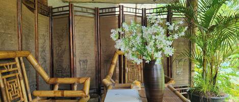 Una habitación con estructura de bambú, un cartel que dice 'Đồng Quy Homestay', una laptop sobre una mesa y un jarrón con flores blancas.
