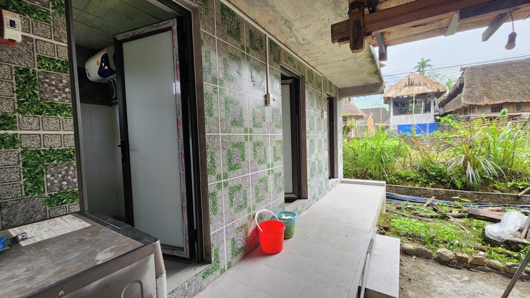 A bathroom with tiled walls, a sink, and a shower area. There is a red bucket on the floor.