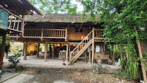 A wooden structure with a thatched roof, a staircase, and a covered outdoor seating area. - Dong Que Homestay-Tours-Motorbike, Car rental, Hiking (Ha Giang 1)