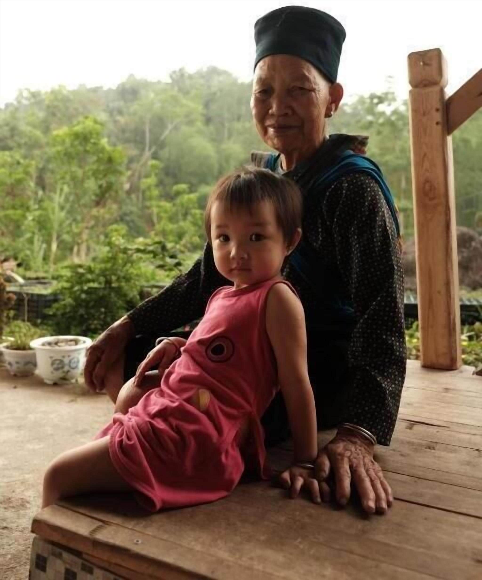 An elderly person sitting on a wooden bench with a child.
