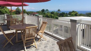 Una terraza con mobiliario de madera y sombrillas rojas, con vistas a un paisaje escénico del océano y la vegetación.