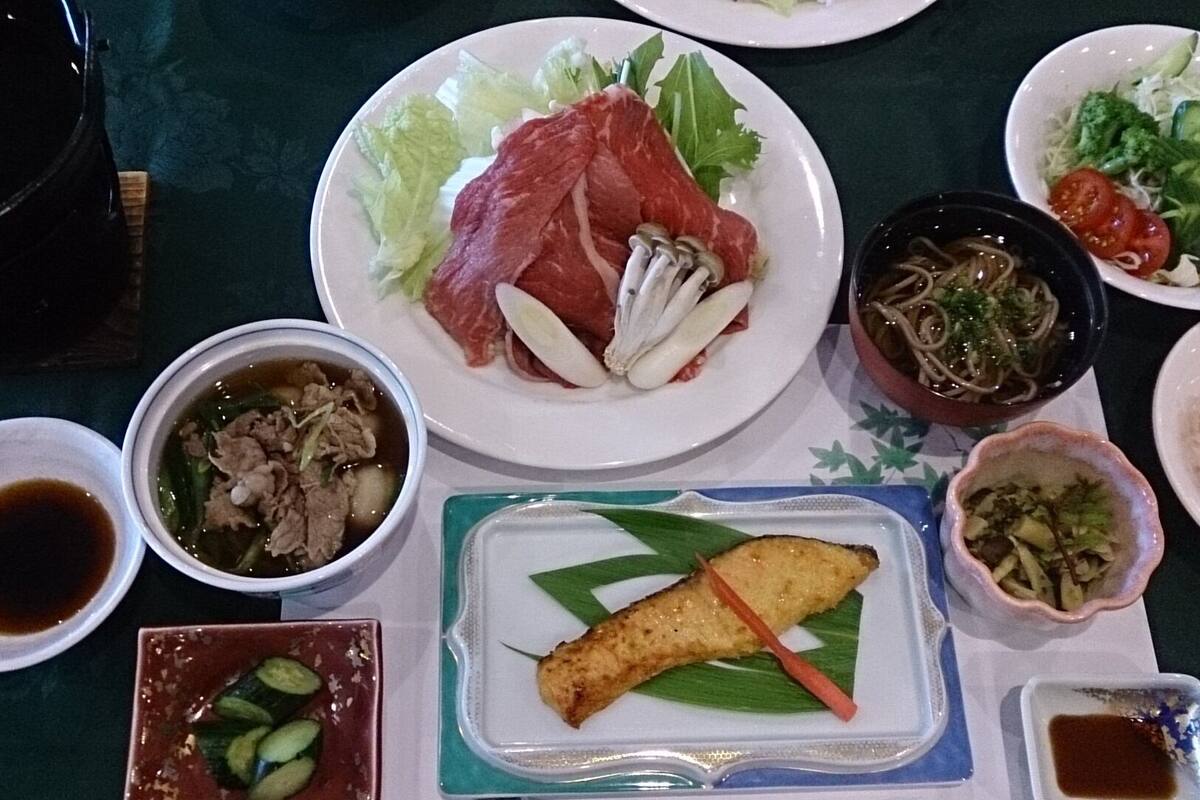 A table with various dishes, including meat, vegetables, and a bowl of soup.