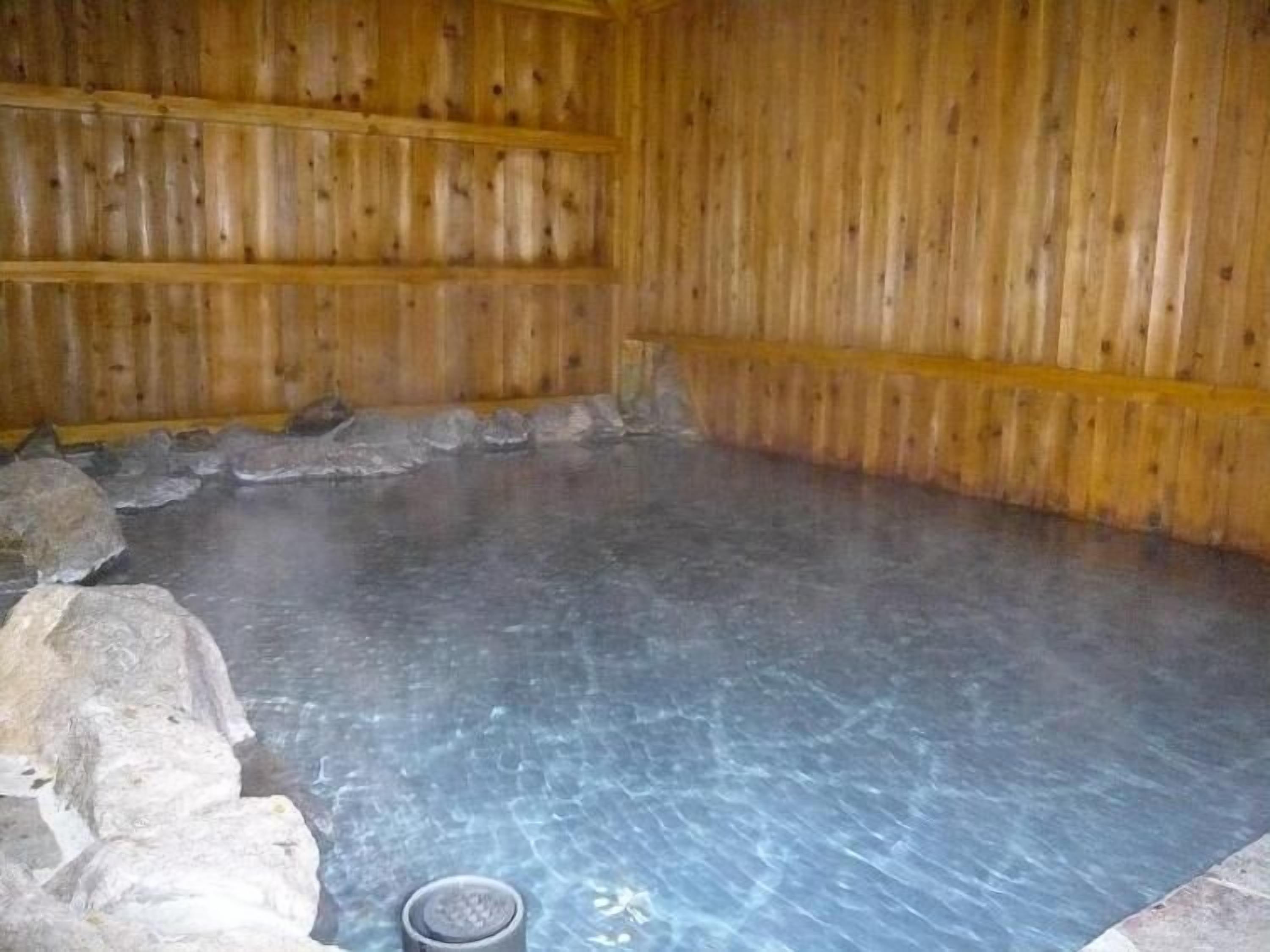 L’intérieur d’un chalet en bois, avec un sol recouvert de pierres et un seau en métal.